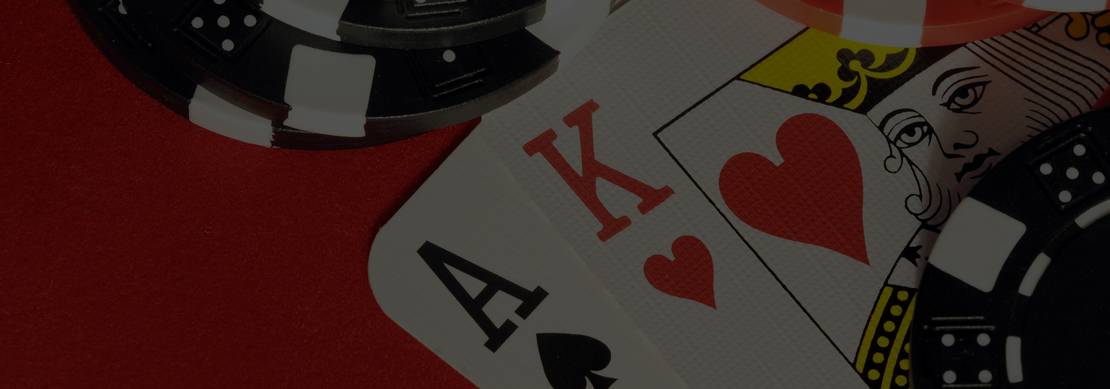 A close-up photo of an ace of spades and king of hearts on a red background with black and red casino chips