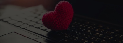 A closeup of a red knitted heart on a laptop keyboard, faded