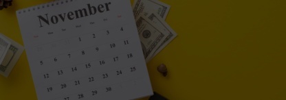 A calendar showing the month of November with dollar bills, a piggybank, a calculator, and pencil on a yellow surface