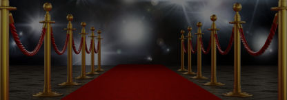 An image of the famous red carpet with red velvet ropes on golden stilts and camera flashes lighting up the dark background
