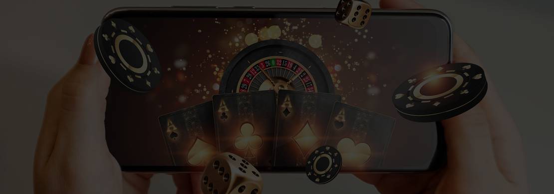 Hands holding a smartphone displaying a roulette wheel and playing cards with gold and black casino chips and dice in the air
