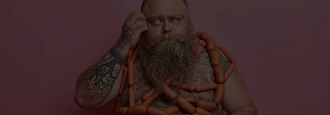 heavily bearded man obsessed with not shaving wrapped in sausages obsessed with eating hot dogs and almost covered with tattoo. 