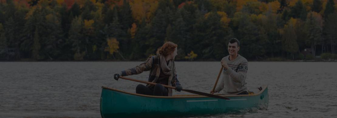 a young couple in a canoe on a mountain lake with a forest full of fall colors in the background