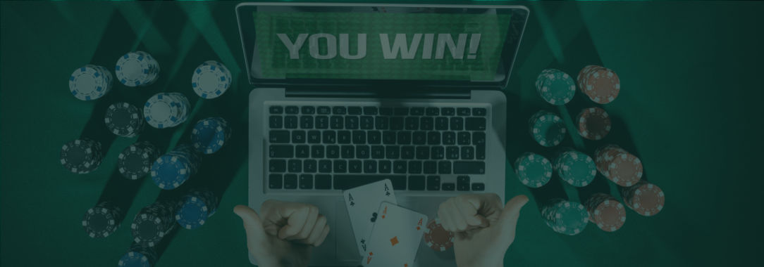 A photo of a man giving two thumbs up sitting in front of a laptop displaying YOU WIN on a poker table with chip stacks
